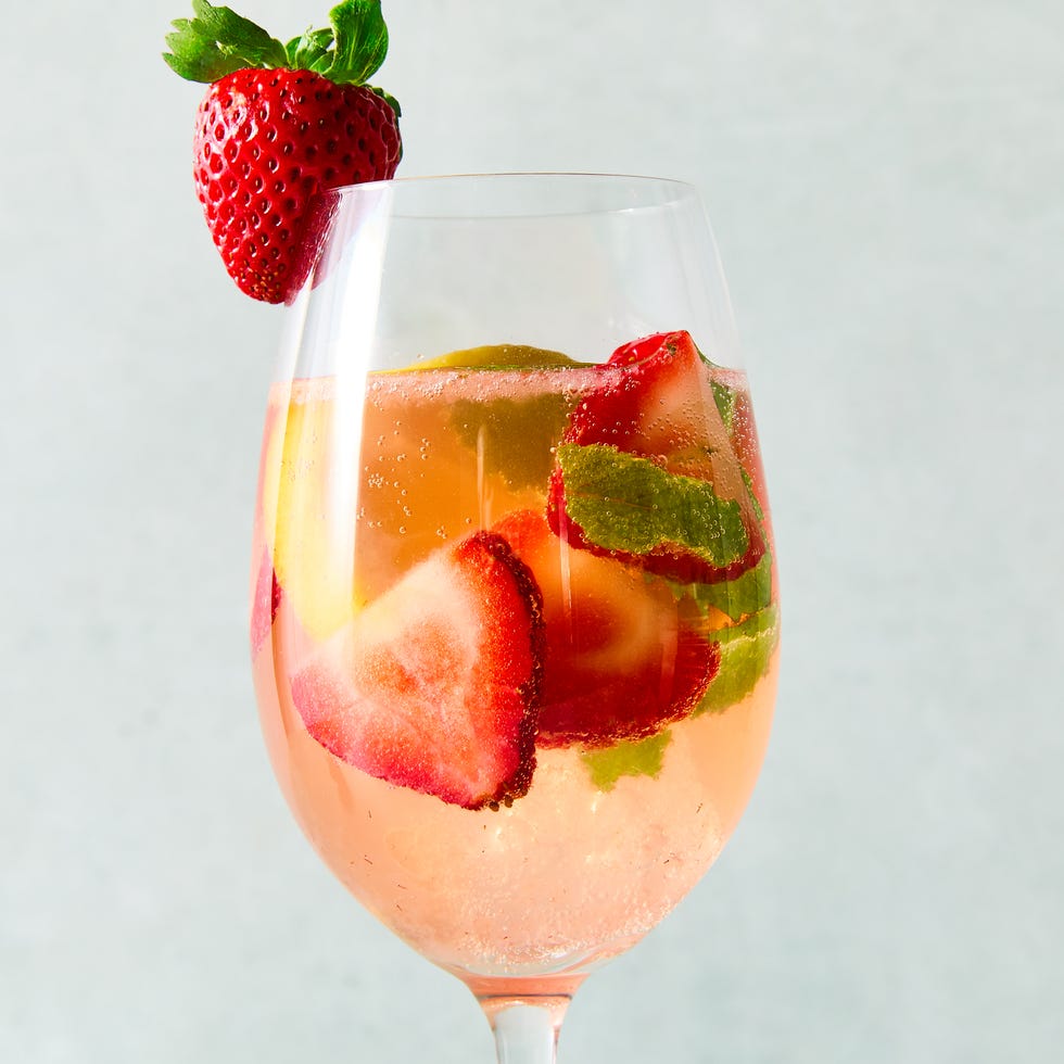 Strawberry Mint Sangria a pitcher and glasses of sangria made with white wine and strawberry syrup with ice, pieces of mint, sliced strawberry, and sliced lemons