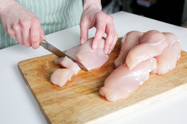 Person cutting chicken breast on wooden chopping board (stock photo)