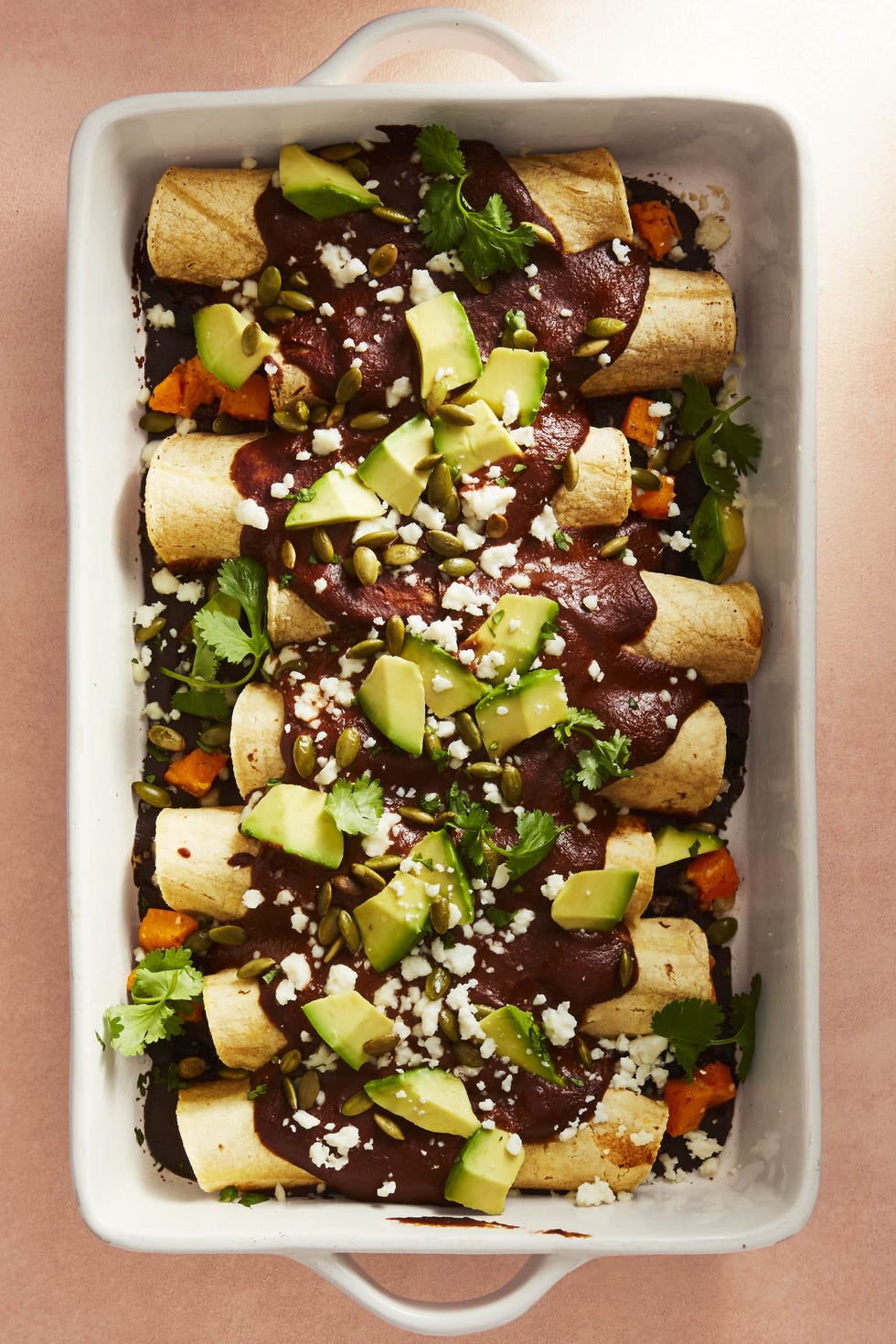 butternut squash mole enchiladas with avocado in a white baking dish
