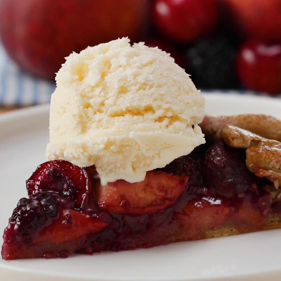 Slice of berry and peach pie topped with vanilla ice cream on a white plate