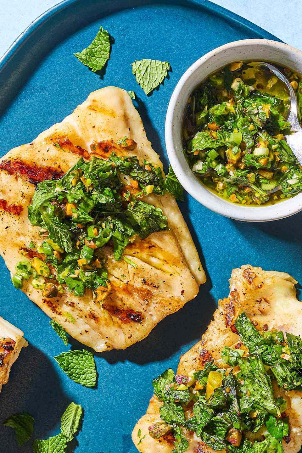 Grilled fish fillets topped with fresh herbs and nuts, served with a side dish of herb sauce, displayed on a blue plate