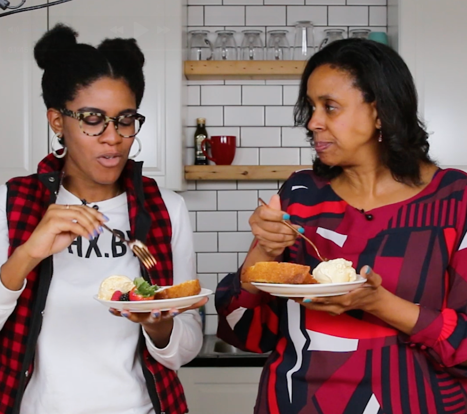 Two people enjoying plates of dessert in a kitchen, engaging in conversation
