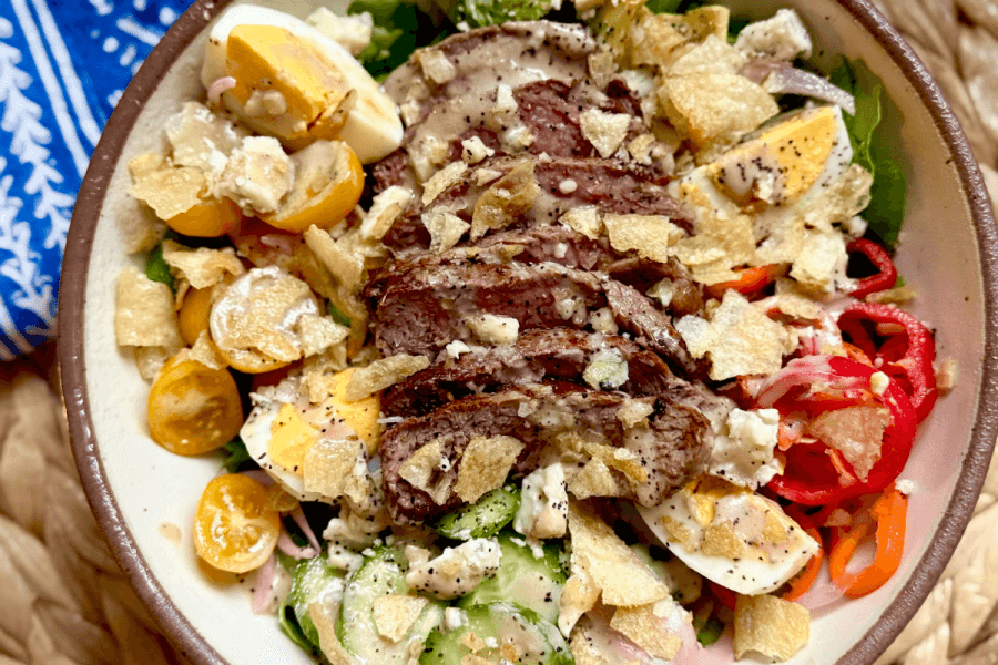 Just in Time for June: Two New Lazy Girl High-Protein Salads (Topped with Chips!) - 2 A delicious Steak Salad ready in just 15 Minutes, featuring sliced steak, cherry tomatoes, hard-boiled eggs, cucumbers, pickled onions, blue cheese, crushed potato chips, and a drizzle of Creamy Balsamic Dressing.