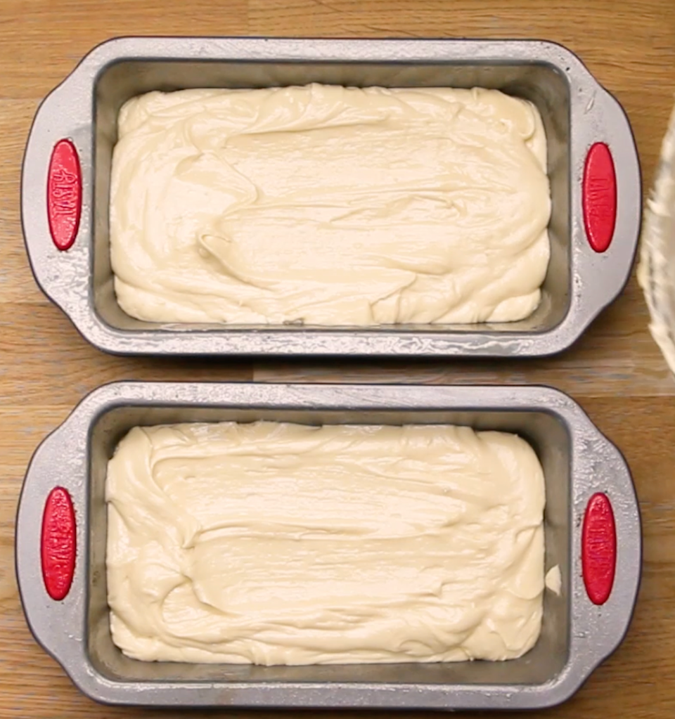 Two loaf pans filled with smooth cake batter rest on a wooden surface, ready for baking