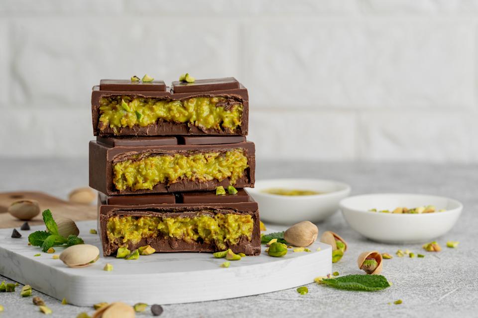 Three stacked chocolate bars filled with a pistachio mixture, placed on a countertop with scattered pistachios and mint leaves