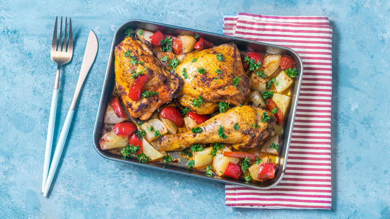 Tray of roast chicken on a bed of root veggies next to a napkin and silverware