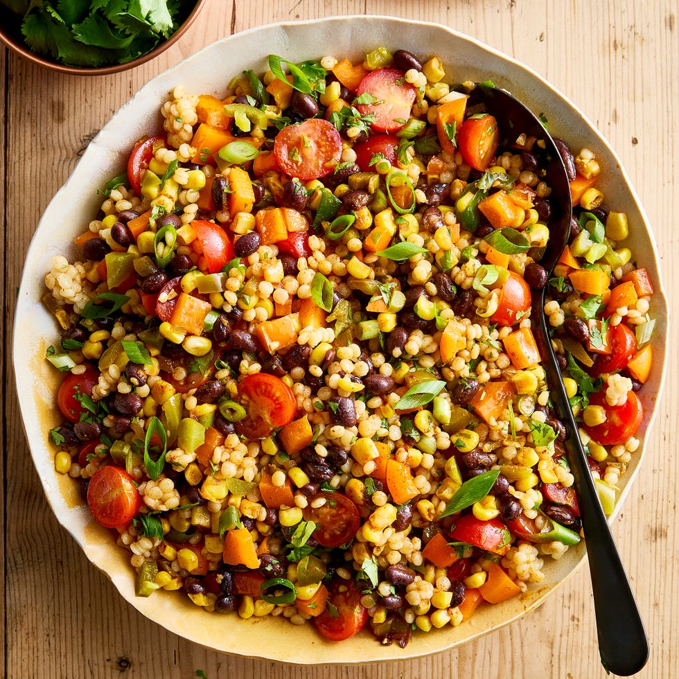Cowboy Caviar Couscous Salad a bowl with pearl couscous, black beans, corn, bell peppers, cherry tomatoes, scallions, cilantro, and pickled jalapenos