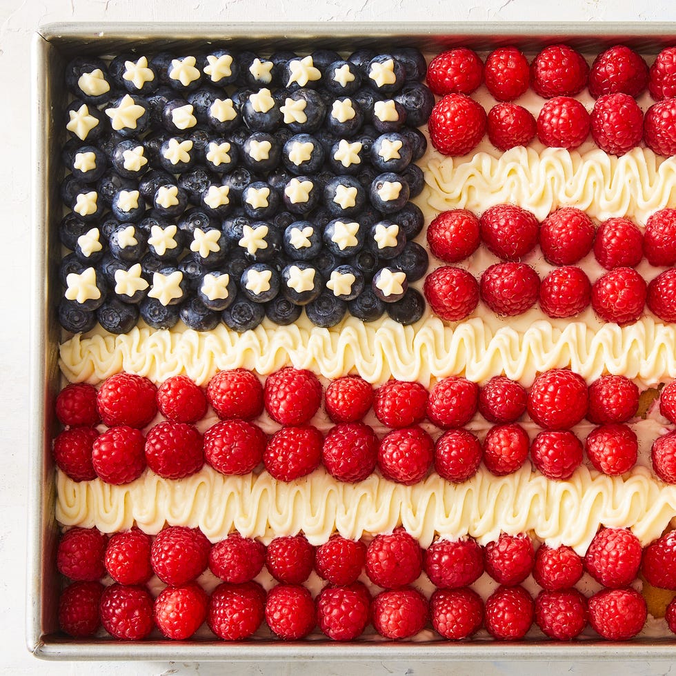 Flag Cake white cake decorated to look like an american flag with blueberries for stars, raspberries for red stripes, and off white frosting for white stripes