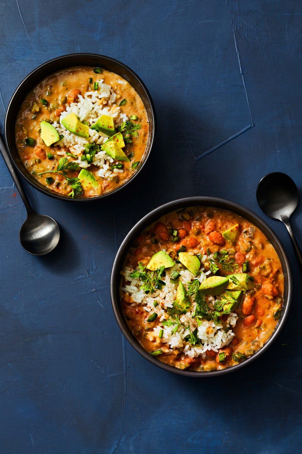two bowls of pinto bean and poblano soup with sliced avocado on top