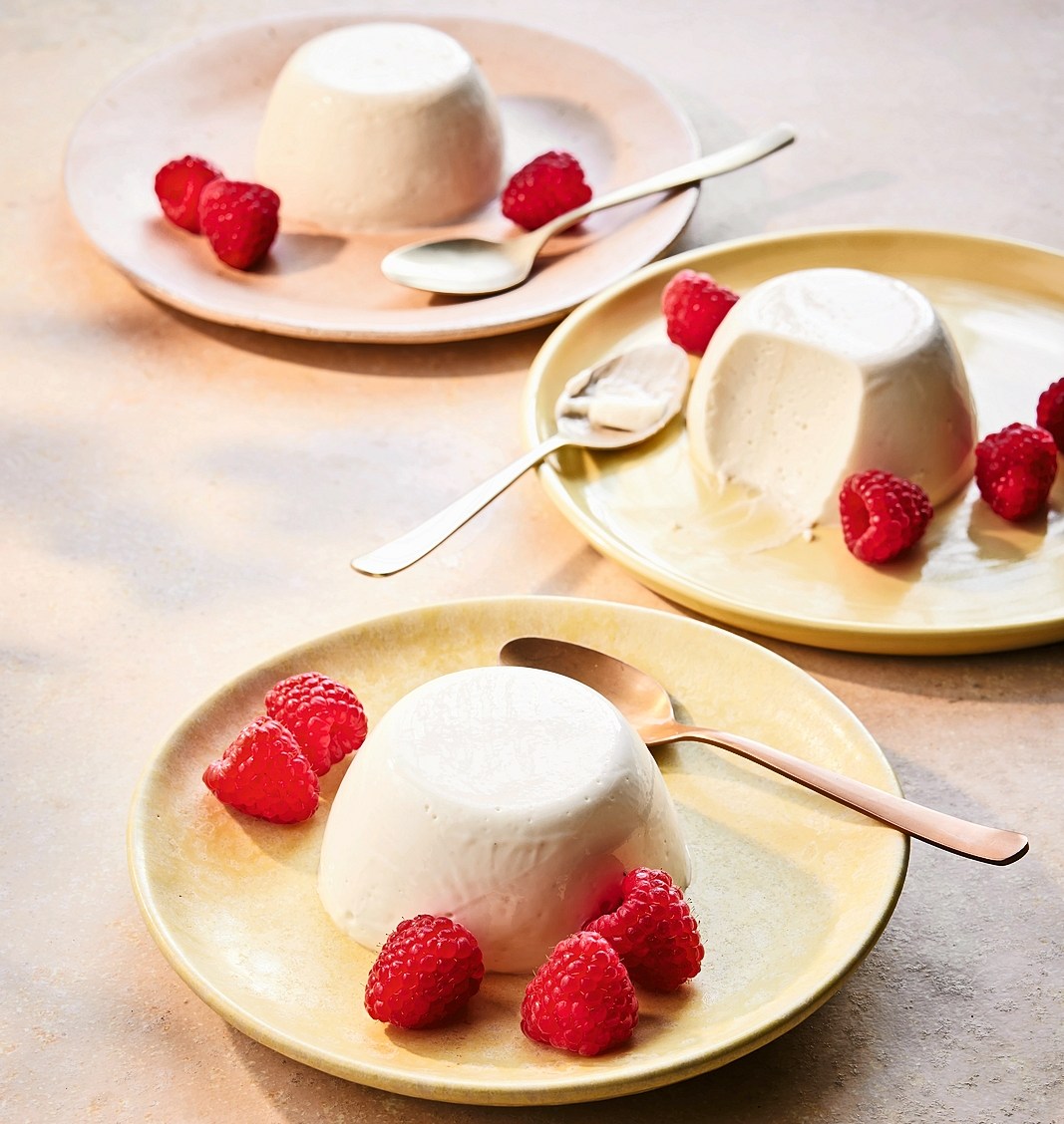 Three panna cotta desserts with raspberries.