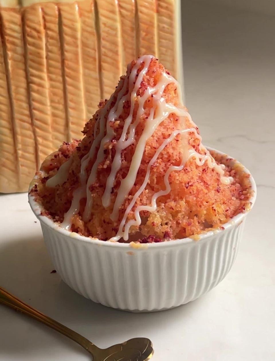 Shaved ice dessert in a bowl, topped with colorful sprinkles and white drizzles, with a plant visible in the background