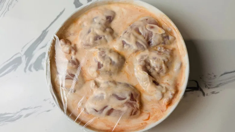 plastic covered bowl with chicken in marinade