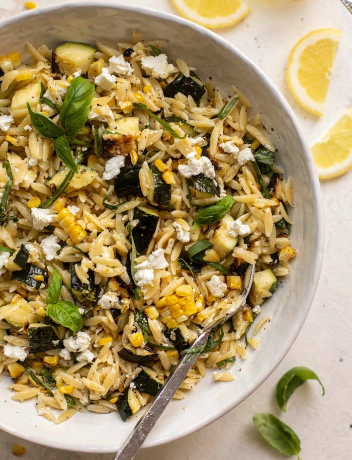 Bowl of orzo salad with corn, zucchini, basil, and feta cheese, garnished with fresh basil leaves
