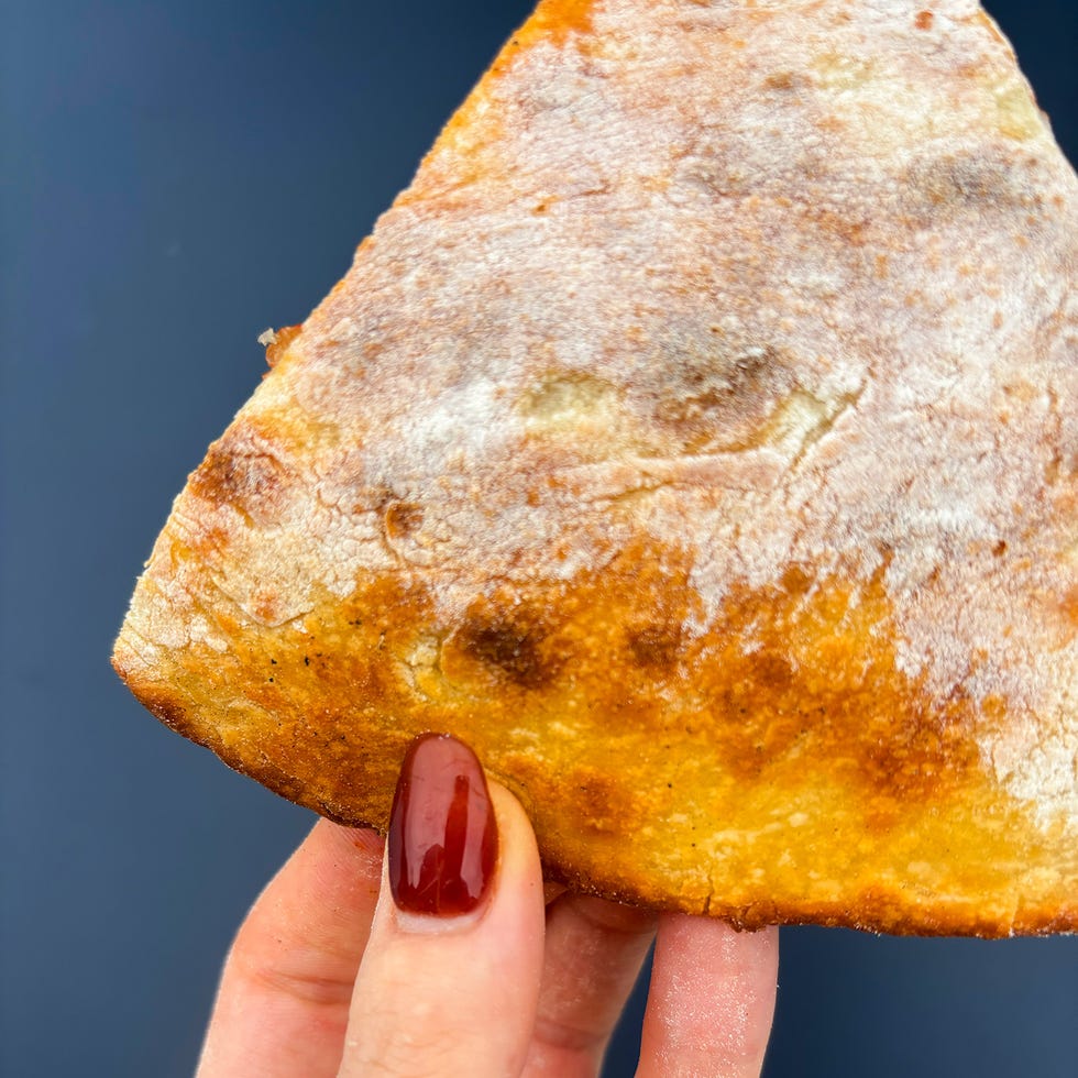 a hand holding a triangular slice of baked bread with golden brown crust