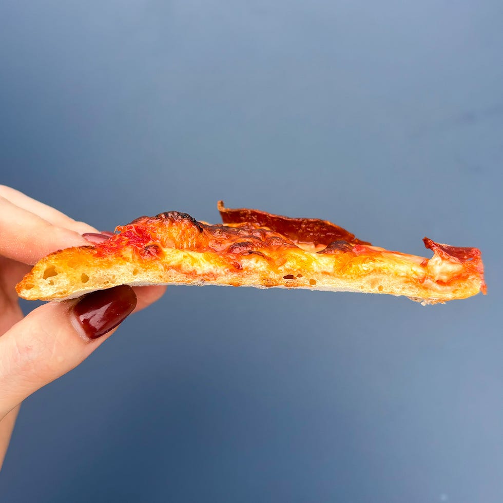 side view of a slice of pizza held by a hand showing crust and toppings