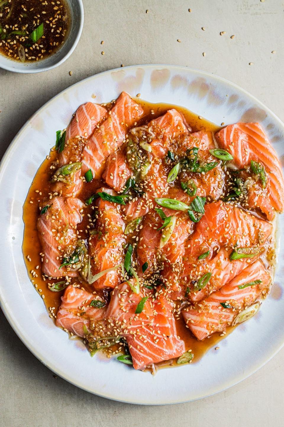 Plate of salmon sashimi with a sesame-soy dressing, garnished with green onions and sesame seeds