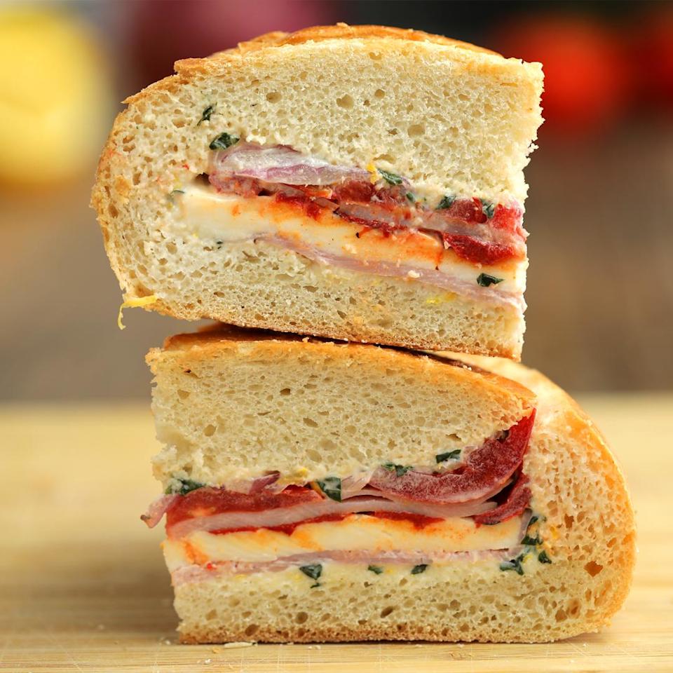 Stacked Italian sandwich with salami, tomato, lettuce, and cheese on crusty bread. Placed on a wooden surface