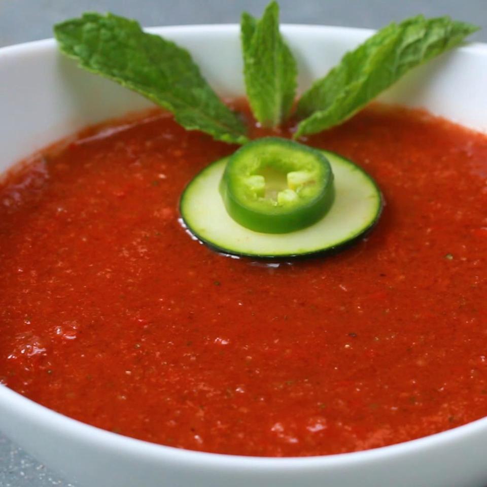 Chilled watermelon soup garnished with fresh mint leaves, jalapeño slice, and cucumber slice in a white bowl