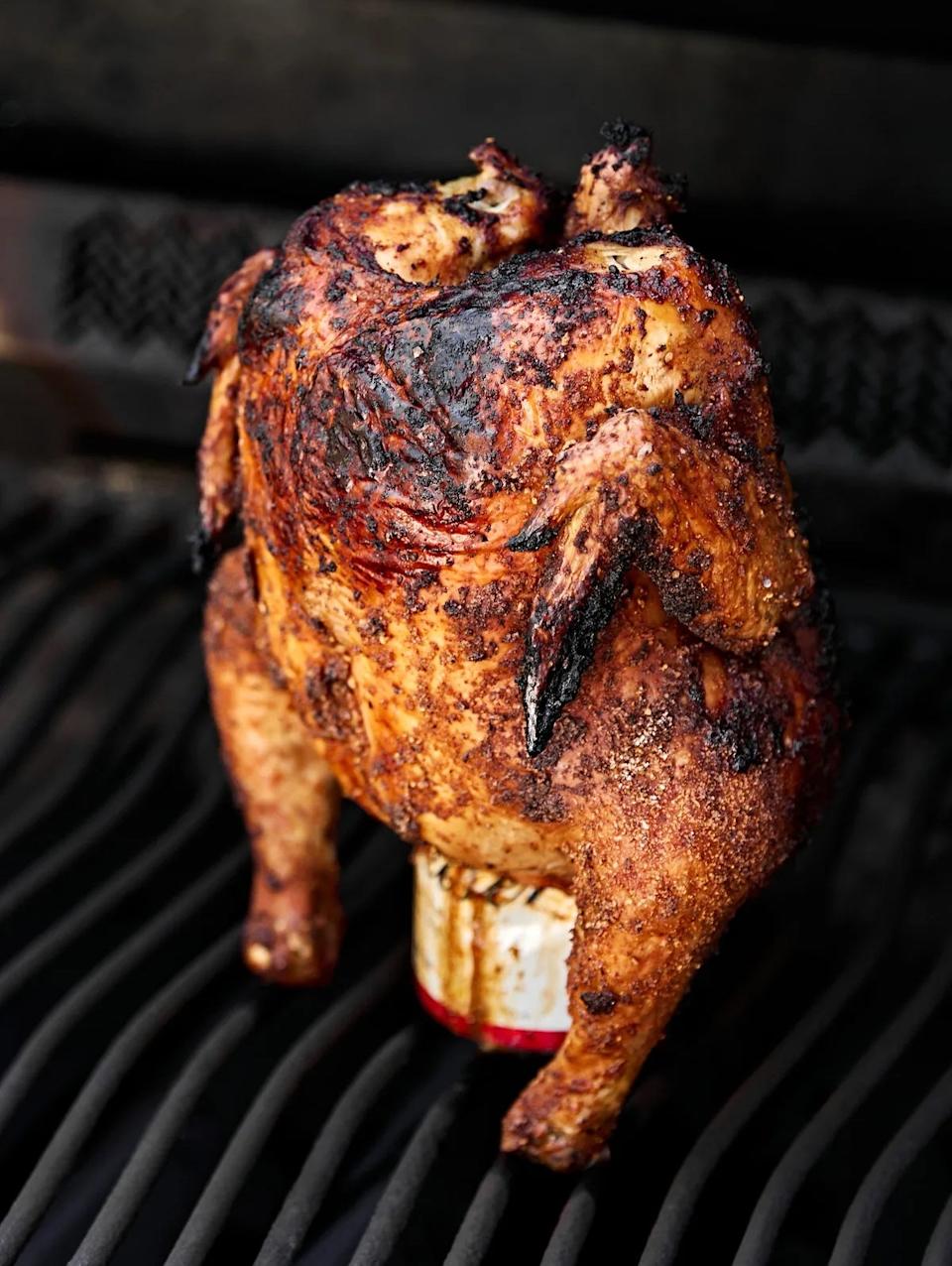 Roasted chicken upright on a grill, balanced on an open can, with crisp skin and charred marks, cooked with a beer-can method