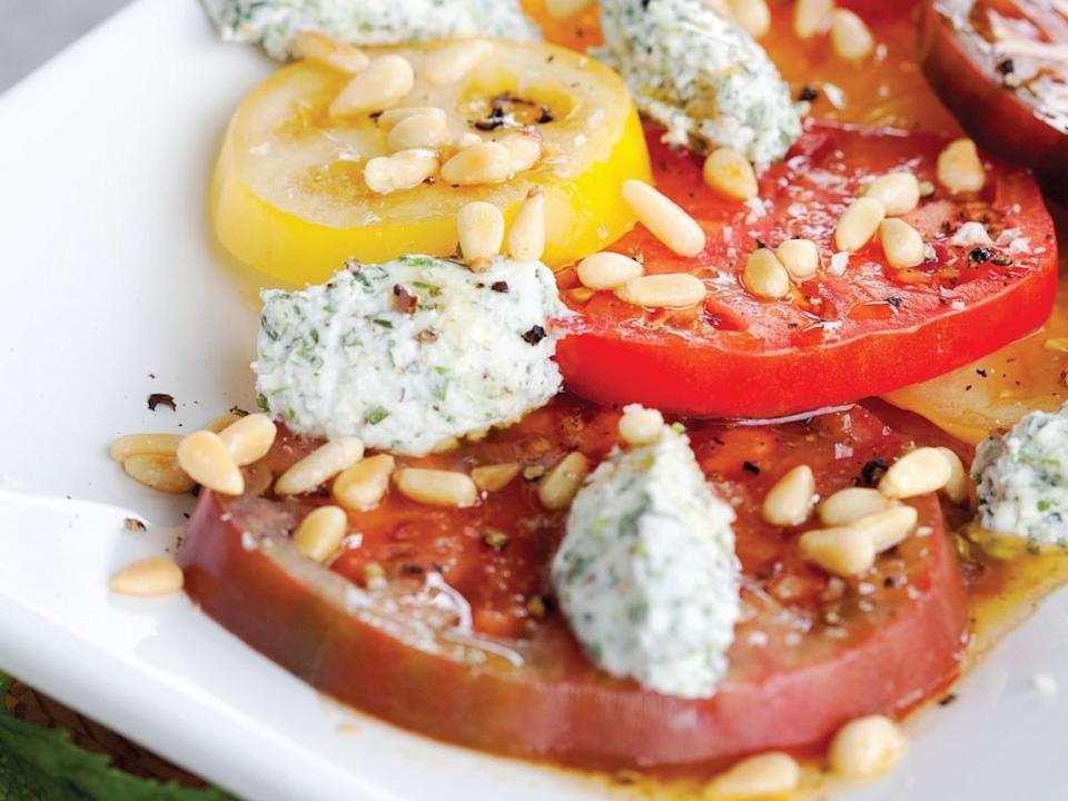 Sliced heirloom tomatoes are crowned by a sprinkling of pine nuts and dollops of herbed ricotta.