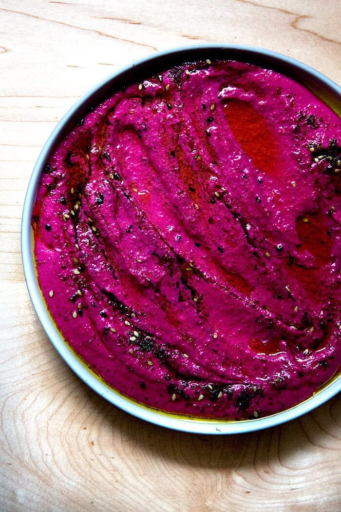 A bowl of creamy beet labneh topped with seeds, showcasing a rich texture on a wooden surface