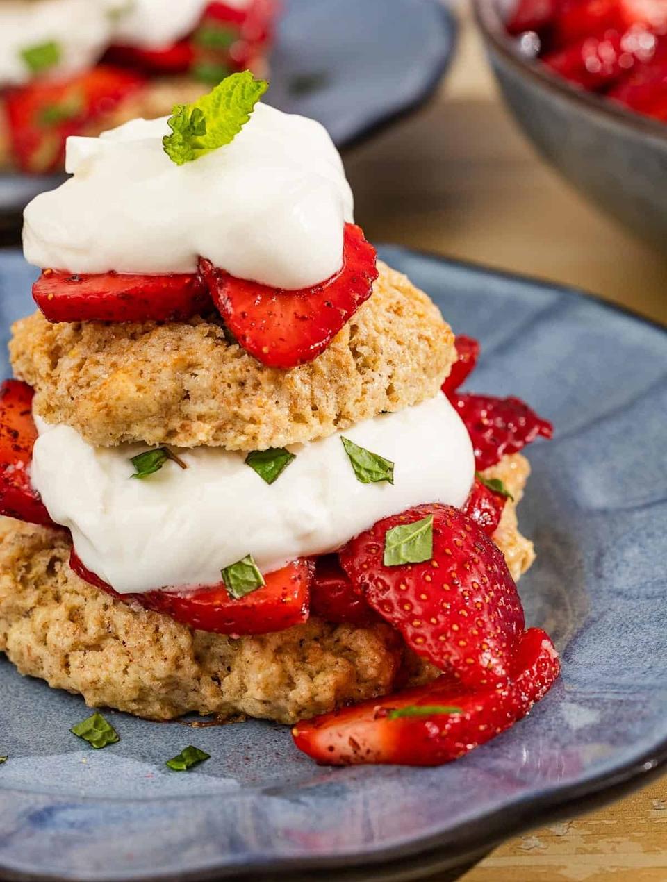 Shortcake topped with whipped cream, fresh strawberries, and mint on a blue plate