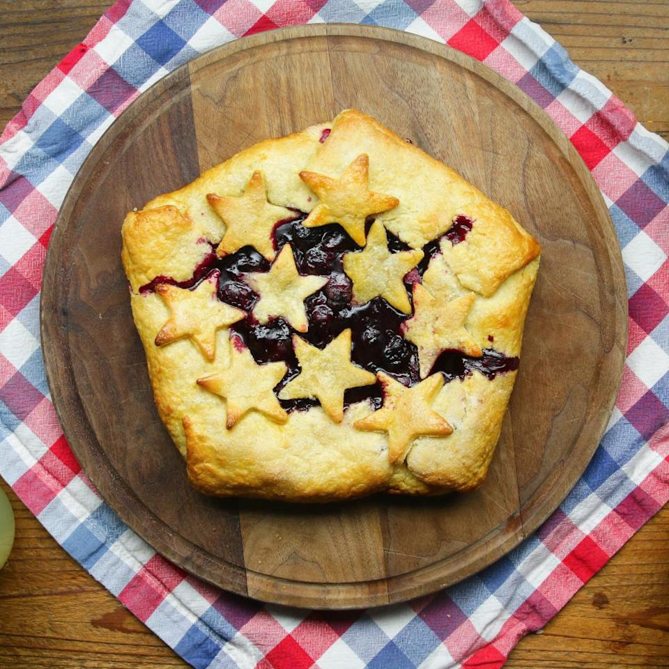 A rustic star-adorned berry galette on a wooden board with a checkered cloth underneath