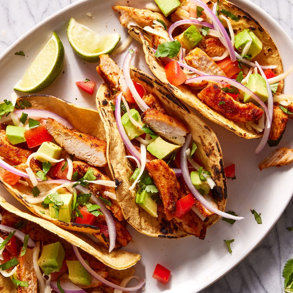 Chicken Tacos flour tortillas on a plate filled with chicken, tomatoes, avocado and red onion