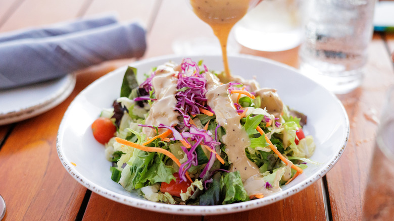 Bowl of salad being dressed on table