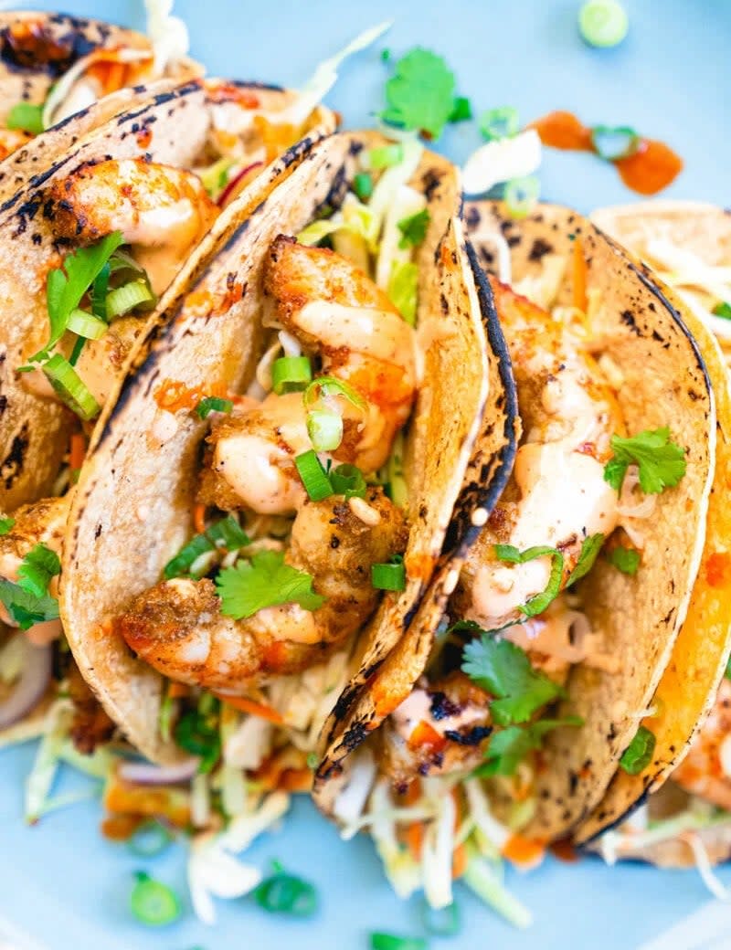 Several grilled shrimp tacos topped with chopped green onions and cilantro on a plate