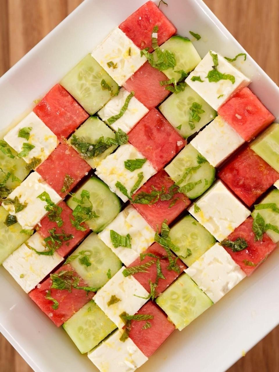 Cubed watermelon, cucumber, and feta arranged in a checkerboard pattern on a square plate, garnished with herbs