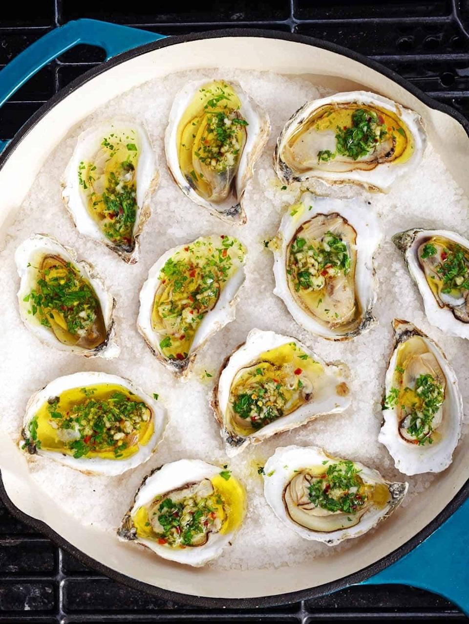 Twelve oysters on the half shell topped with a herb and garlic mixture, arranged on a bed of salt, ready for serving