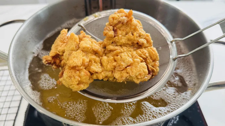 removing fried chicken from oil with slotted spoon