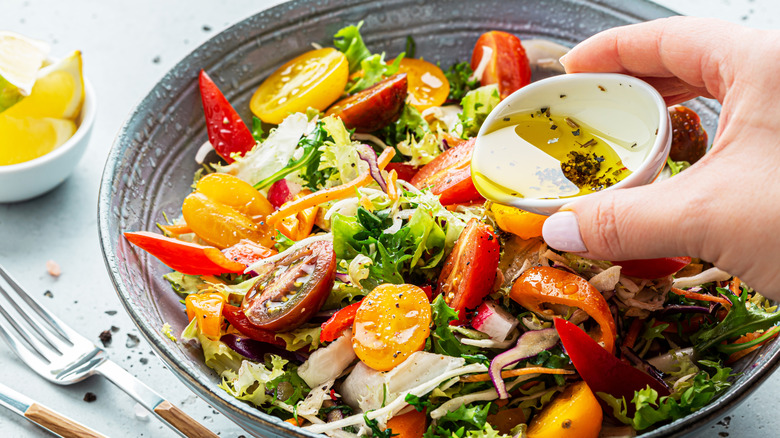 Adding dressing to salad bowl with lettuce and tomatoes