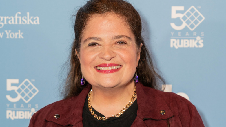 Alex Guarnaschelli smiling in maroon jacket with gold necklace