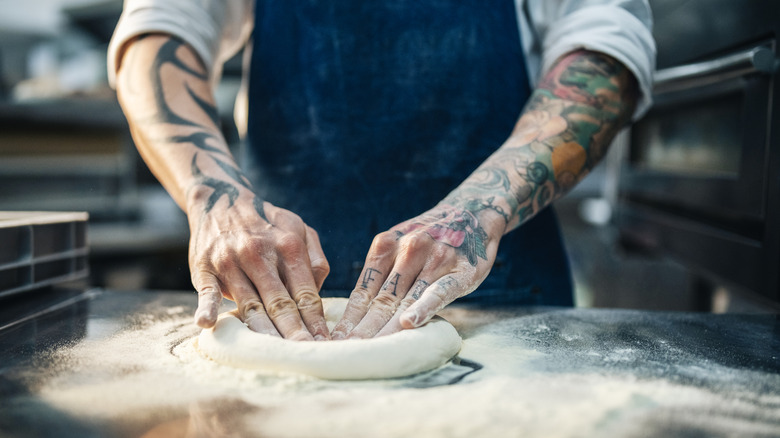 A person's hands are seen shaping pizza dough on a heavily floured counter.