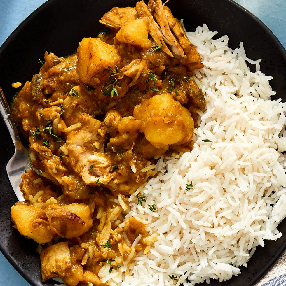 black plate of jamaican chicken curry over white rice on a blue background