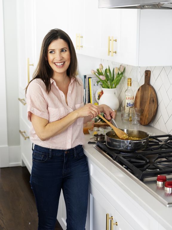 Woman cooking in a kitchen stirring a dish on the stove smiling and standing near a counter