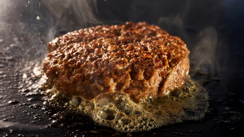 Burger patty with butter cooking on a stove