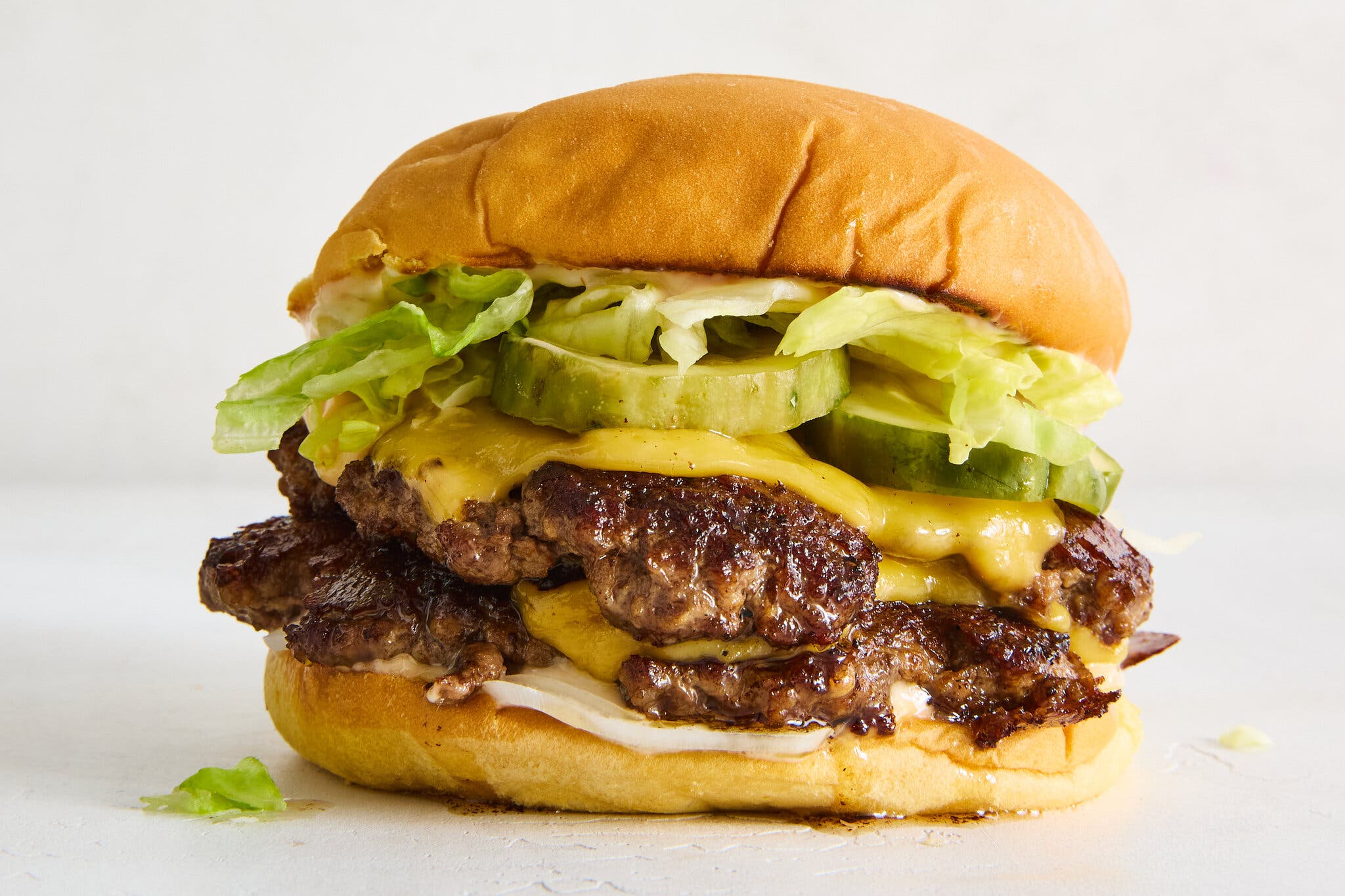 A side image of a smash burger topped with cheese, pickles and lettuce. 