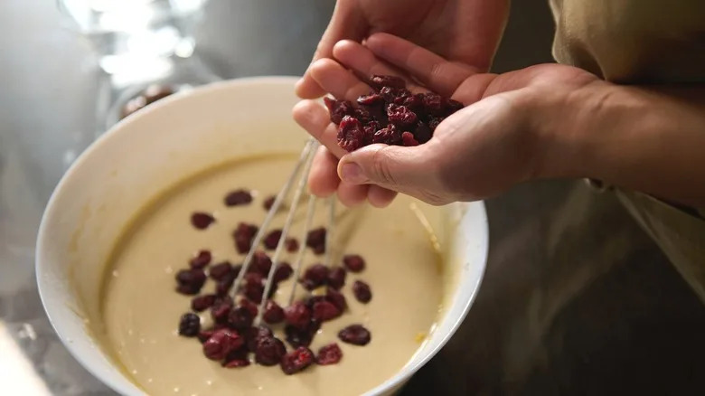 Person adding fruit to bowl of batter