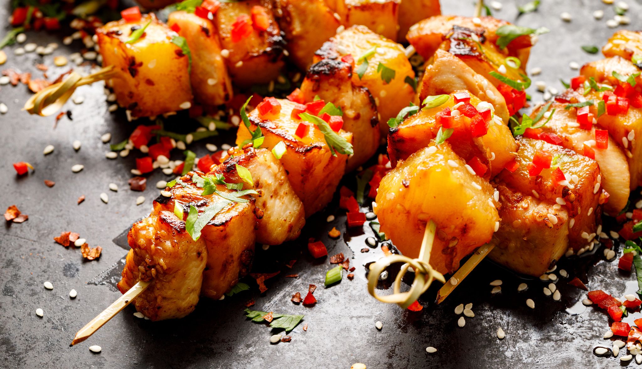 Yuzu kosho chicken skewers with grilled pineapple are pictured. The skewers are garnished with sesame seeds.