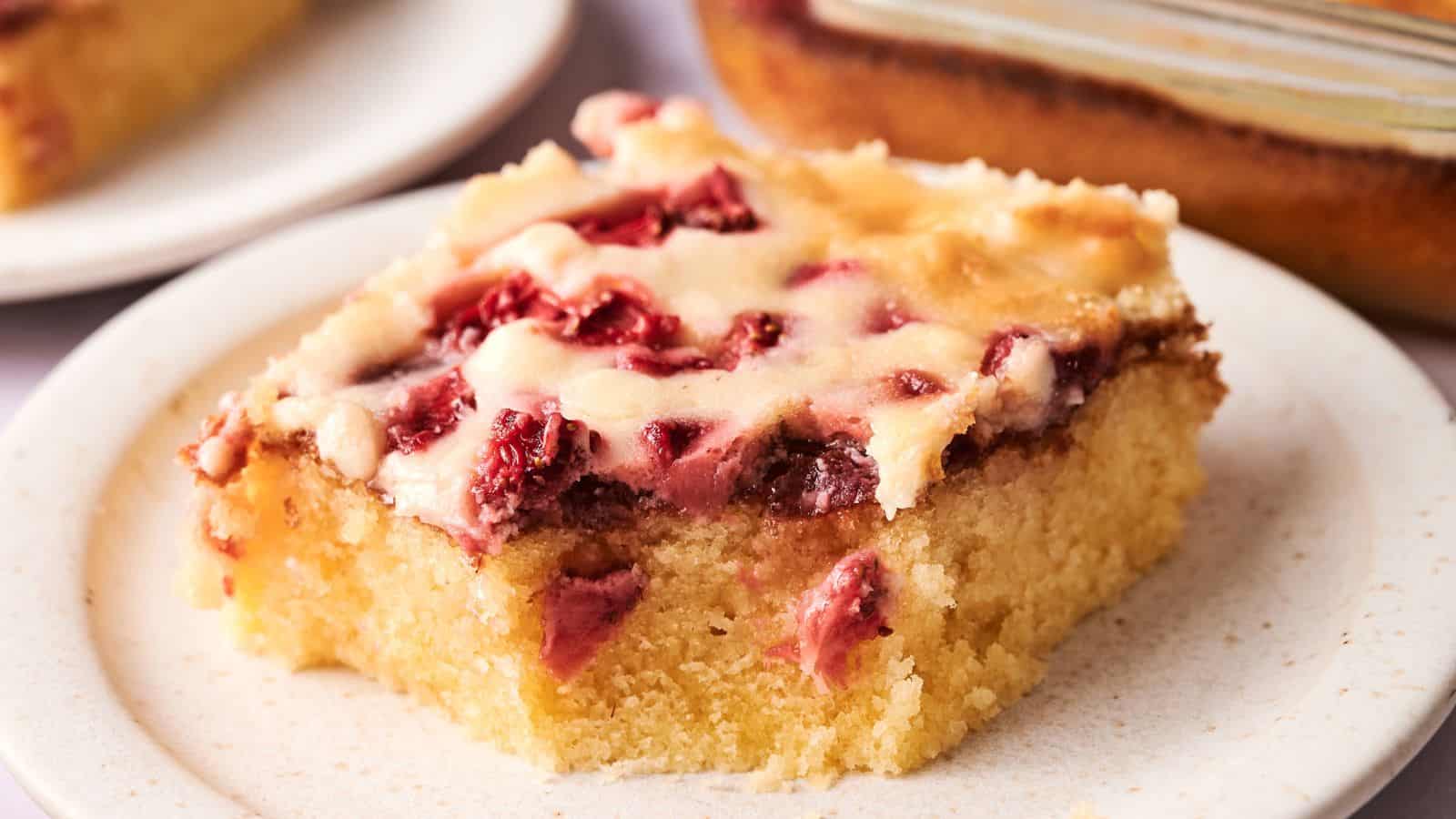 A slice of cherry-topped cake with a creamy layer, served on a white plate.