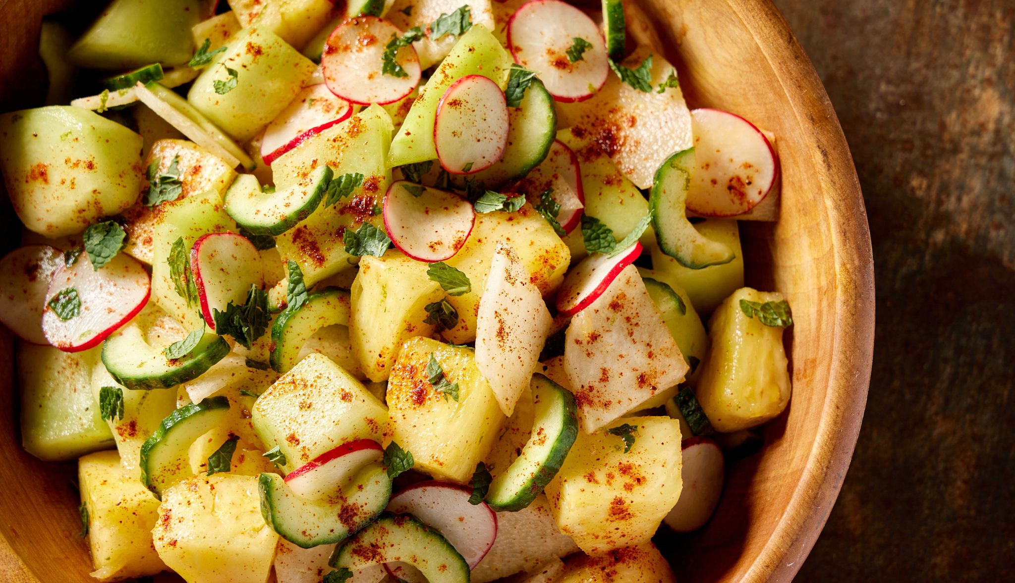 A chili-lime pineapple and honeydew salad is pictured in a bowl atop a countertop