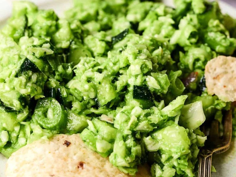 A close-up of chunky guacamole with pieces of jalapeño, onion, and tortilla chips visible.