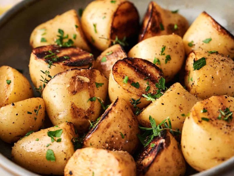 A bowl of roasted potatoes cut in halves, garnished with chopped parsley and black pepper.