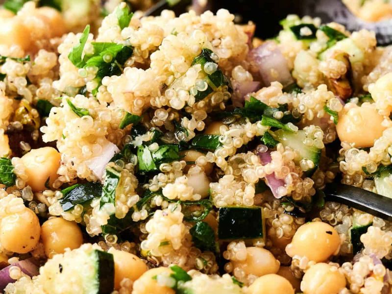 Close-up of a quinoa salad with chickpeas, diced cucumber, red onion, parsley, and herbs, mixed together.
