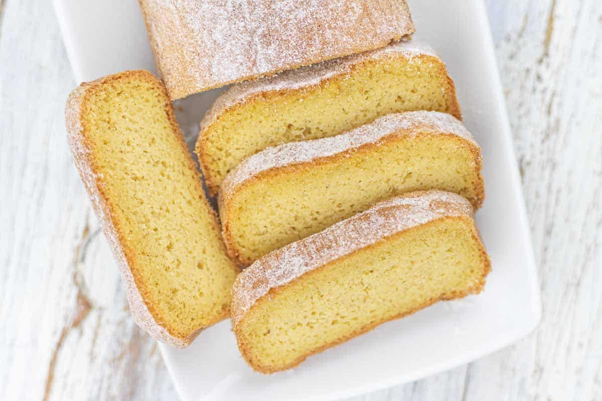 A sliced loaf of vanilla cake dusted with powdered sugar.