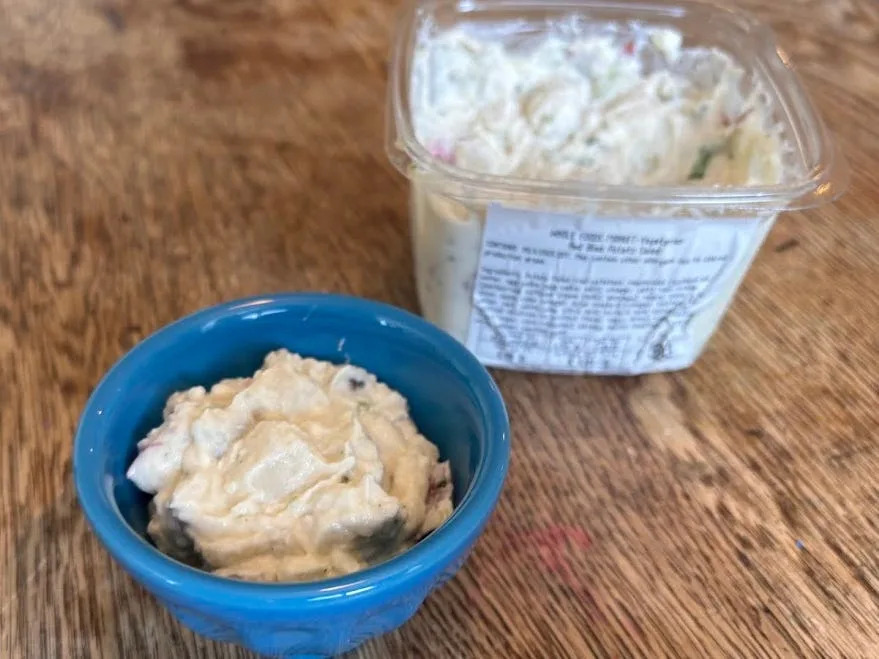 A small blue bowl of Whole Foods Red Bliss potato salad next to the container.