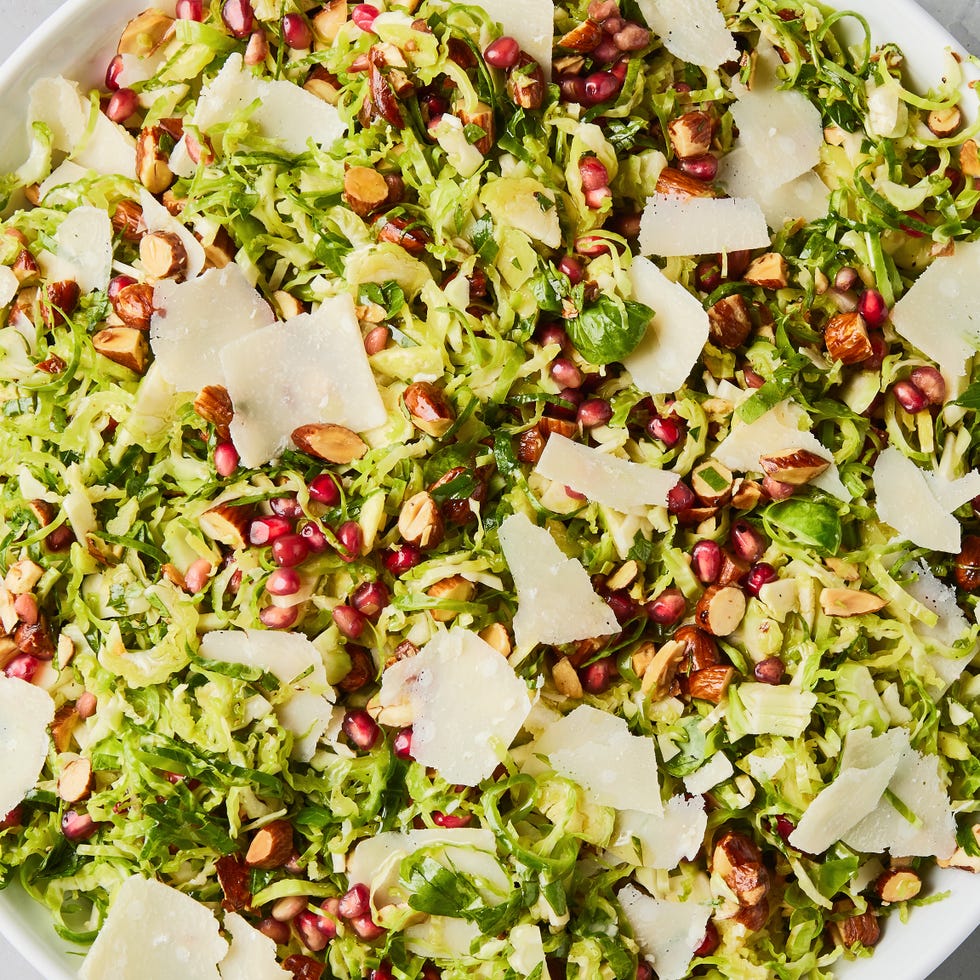 Brussels Sprouts Salad shaved brussels sprouts with pomegranates, shaved parmesan, and chopped toasted almonds in a white bowl